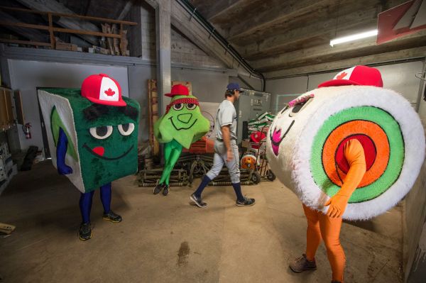 An Everrett Aquasox player walks by the "Sushi" mascots while they wait under the stands before racing around the bases during a game between the Vancouver Canadians and the Everett Aquasox at Nat Bailey stadium.