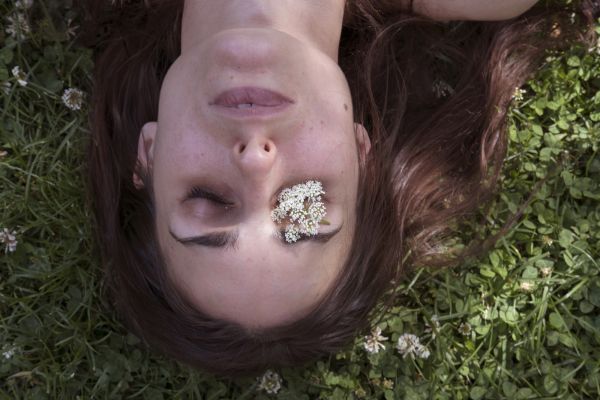 Rebecca, who nearly always needs a cane due to brain trauma injury and the permanent paralysis, though low level, poses on grass with flower, in New York