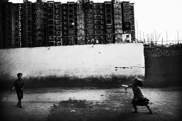 Uighur children play badminton near the construction site of high-storied modern buildings where a large scale of Uighur old communities once existed.