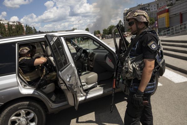 Ukrainian police officers prepare to escort and assist with the delivery of humanitarian aid on the north eastern edge of Kharkiv as smoke rises from a Russian grad rocket attack in a village just north of their location.
