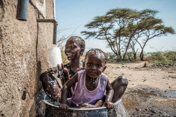 Evelyn Ekutan (11) plays with her sister Stella Ekutan (2) in a bucket of water underneath the kiosk's tap in the remote region of Turkana, Kenya.