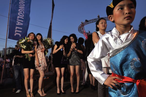 Fashion models and a traditional child acrobat await the arrival of the pop band Camerton at a concert at the APU vodka and beer factory.