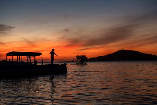 Tuesday, December 13th, 2022: Honduras, Cayos Cochinos, Local Boy Fishing from a boat at Sunset with a view of Cayo Menor taken from Cayo Largo.