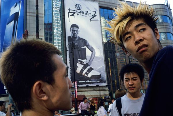 Young men, including a student with bleached blonde punk styled hair, idle their time away at the Shengli Shopping Square in Dalian, Liaoning, China, A Nike advertisement featuring Lebron James covers a department store behind them.