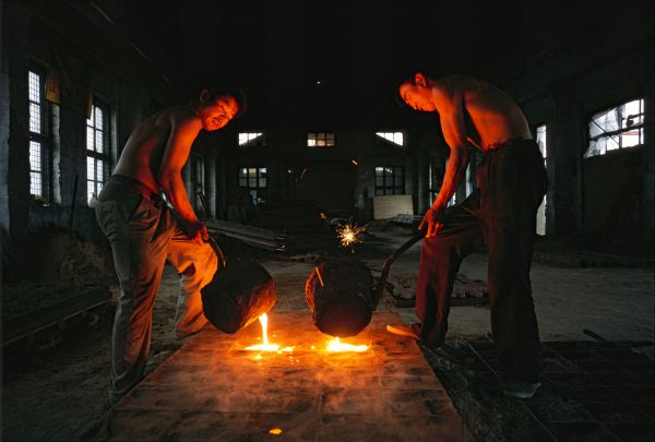 Two workers ladel molten metal into a fence mold at the Shenyang Tiantsu Foundry Company in Shenyang, China.